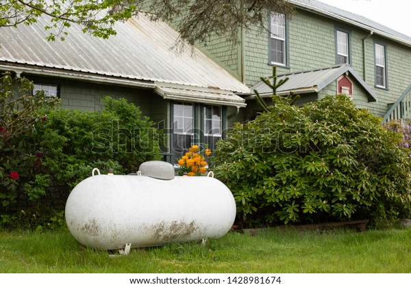 Large propane\
tank in the yard of a rural home, with a house in the background\
and space for text on the\
right