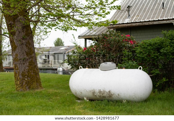 Large propane tank in the yard of a rural home,\
with space for text on the\
left