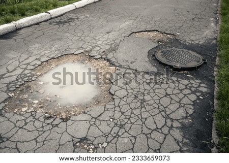 Large puddle of muddy water next to a sewer manhole in the middle of an asphalt road