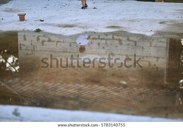 large puddle with the reflection\
of the boy. puddle on the concrete and there are several\
pipes
