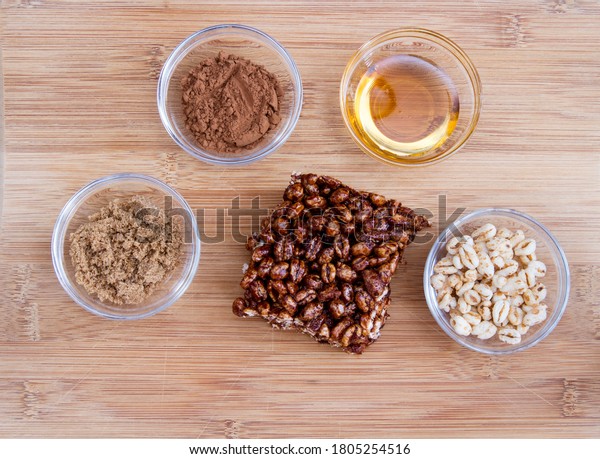 Large\
puffed wheat square treat with small glass bowls of raw ingredients\
beside; delicious and chewy puffed wheat\
squares