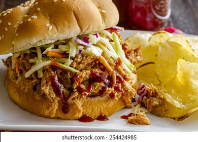 Large Pulled Pork Barbeque Sandwich With Coleslaw Sitting On White Plate With Potato Chips On The Side