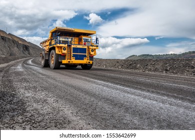 Large Quarry With Many Horizons And Ledges. Gravel Road Located On A Rocky Ledge. Mining Truck Is Driving Along A Mountain Road.