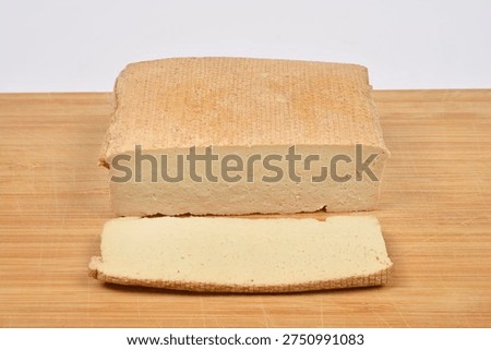 A large rectangular block of smoked tofu with one thin slice cut off and placed in front on a natural wooden cutting board