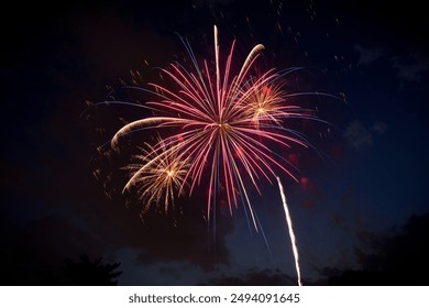 A large red and blue firework and two smaller yellow gold fireworks at dusk against a partially cloudy night sky. Copy space.