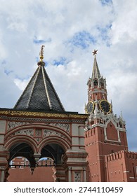 Large red brick building with a clock tower and a steeple. The clock tower has a large clock face and a star on top. The building is surrounded by a courtyard with a stone staircase leading up to it