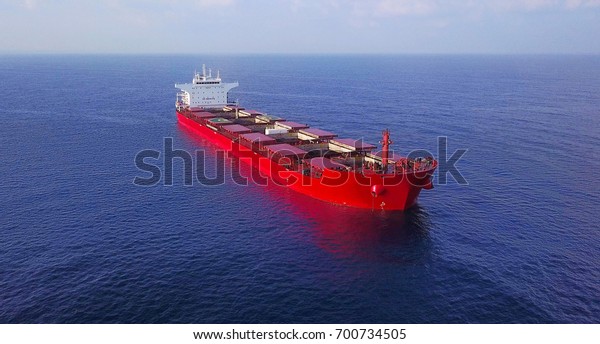 Large red bulk oil\
carrier ship sailing / docking in open ocean near large power\
station - aerial view