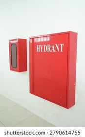 A large red hydrant box and a smaller fire extinguisher cabinet mounted side-by-side on a plain white wall for emergency safety. Ideal for fire safety and building security presentations.