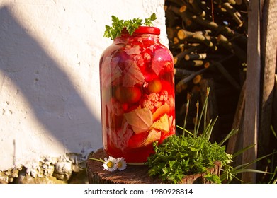 Large Red Jar With Assorted Pickles: Red Beets, Cauliflower, Cabbage, Green Tomatoes. Pickle Jar With Vegetables In Red Brine Surrounded By Parsley On Wooden Stump.