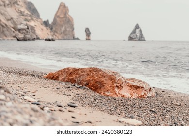 Large red jasper rock on the beach, with the sea in the background. Big Red Jasper Stone Close Up