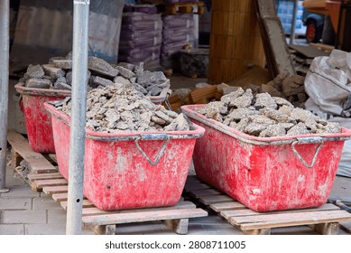 Large red plastic construction tubs filled with concrete rubble and debris on wooden pallets, renovation and building waste management site.