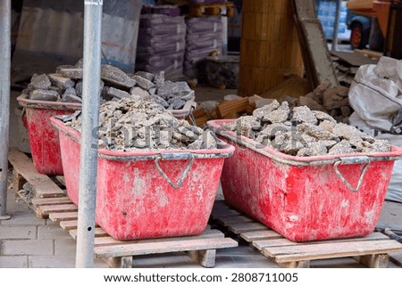 Large red plastic construction tubs filled with concrete rubble and debris on wooden pallets, renovation and building waste management site.