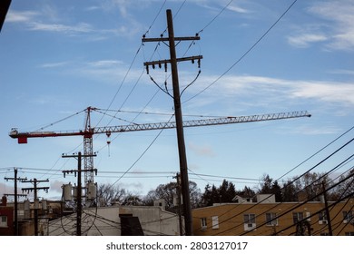 Large red tower construction crane and multiple wooden utility poles with intricate electrical wires standing prominently above various buildings in a densely wired urban landscape under a light blue sky, illustrating city infrastructure and ongoing development.