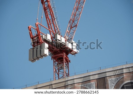 A large red tower crane is positioned above a building under construction, its counterweights visible against the bright sky