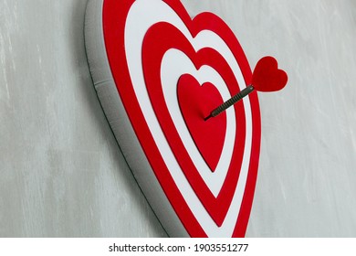 Large red and white heart as a dartboard with an arrow in it 