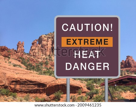 Large road warning sign saying CAUTION! EXTREME HEAT DANGER with stone mountain and deep blue sky background. Climate change concept.