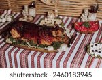 A large roast pig is on a wooden platter on a table with other food items. The tablecloth is red and white striped