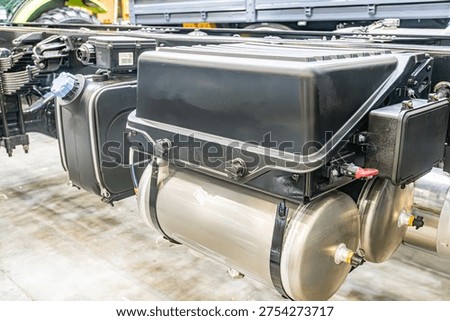A large, robust engine or generator unit in an industrial setting, primarily black with lighter areas from maintenance Metallic structures and pipes visible Overhead lighting casting shadows Docum