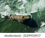 A large rock is in the ocean with waves crashing around it. The rock is surrounded by water and he is a part of the ocean floor. Concept of strength and stability