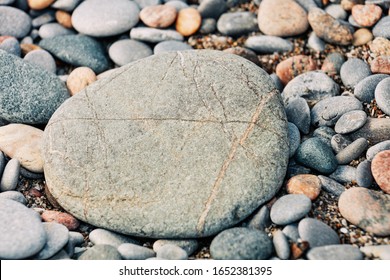 A large rock set amongst many smaller rocks on a sandy beach 