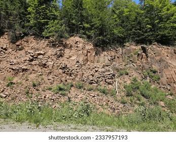A large rock wall along a road with a forest above it.