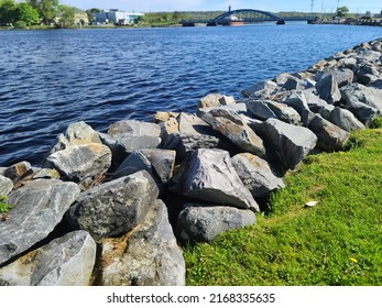 A Large Rock Wall Extending Along A Path Next To A River.