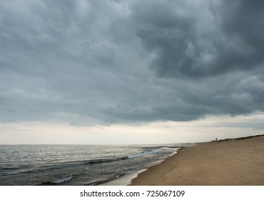 Large roiling dark clouds fill the sky and half the image. Below them, warm light punches through in the distance. It  feels like hope in the is dusky ocean scene.