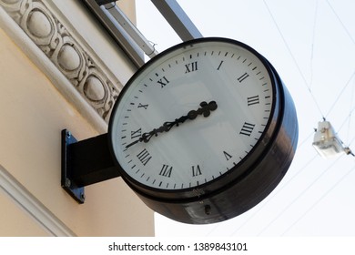 large round clock with an arrow on the wall of a building