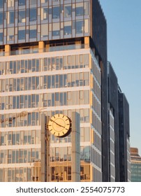 Large round dial on two pillars. In the background a mirror skyscraper. Rectangular windows contrast with the shape of the clock. Urban landscape. Megacity. Walking in Warsaw.