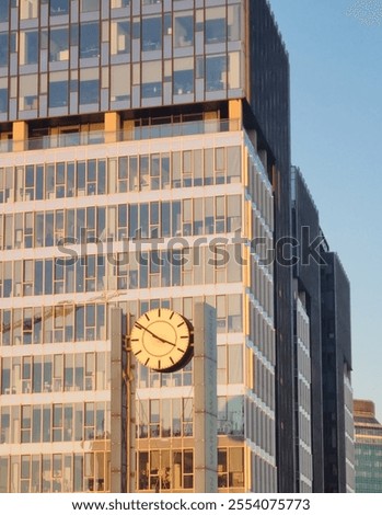 Large round dial on two pillars. In the background a mirror skyscraper. Rectangular windows contrast with the shape of the clock. Urban landscape. Megacity. Walking in Warsaw.
