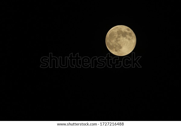 A large round full moon with a visible texture in the\
black night sky