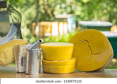 Large round pieces of natural beeswax on the background of beehives in the garden. Large round pieces of beeswax, bee smoker and beekeeper's tool on the background of beehives in the garden. - Powered by Shutterstock