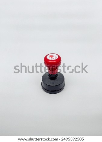 A large round plastic stamp with a red handle, photographed from the upper side in an upright position.