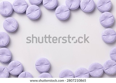 Large, round purple chewable tablets create a frame around sides of a white background.