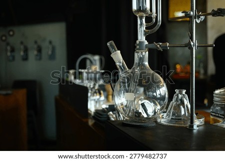 A large round-bottom flask connected to distillation glassware sits on a dark lab bench, ideal for science, chemistry, and research concepts.