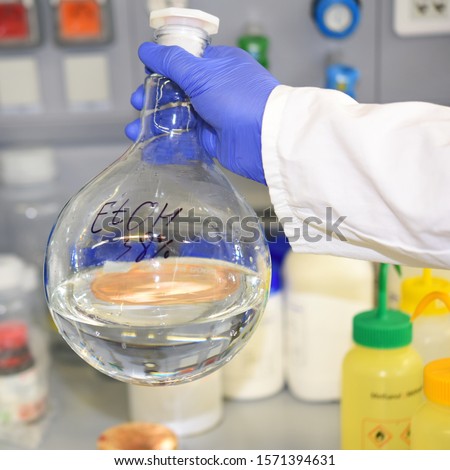 Large round-bottom flask flask with ethanol in the hands of an employee of the laboratory on the background of the working surface. Alcohol. Spirit.
