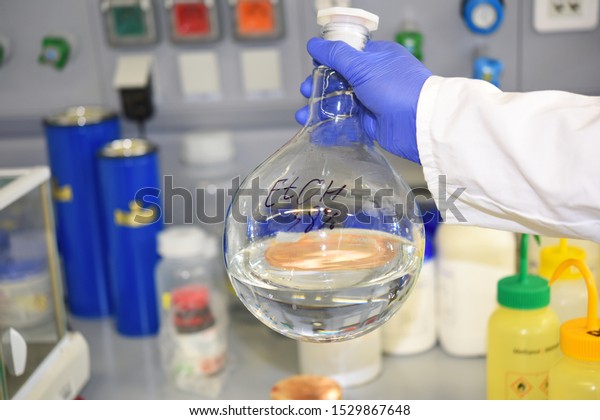 Large round-bottom flask flask with\
ethanol in the hands of an employee of the laboratory on the\
background of the working surface. Alcohol.\
Spirit.