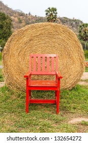 Large rounded hay stack on green grass with red chair in front, taken outdoor