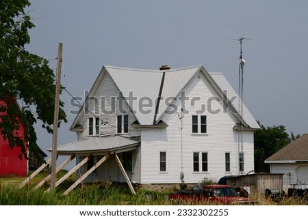 a large rural farm house with a porch roof supported by wood beams on a sunny summer day