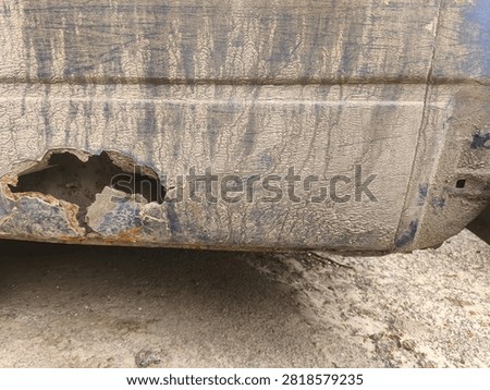 A large rust hole has formed in the lower side panel of an older van, exposing extensive corrosion caused by years of moisture and environmental exposure. Peeling metal and oxidized surfaces highlight the importance of preventative maintenance and timely body repairs. The image is ideal for automotive restoration, corrosion analysis, vehicle inspection, transportation maintenance, insurance documentation, mechanical servicing, and educational content about metal deterioration.