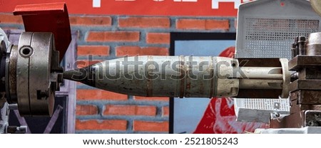 A large, rusted missile is clamped securely within a metal vise. The missile is partially visible, with the front end protruding towards the viewer. 