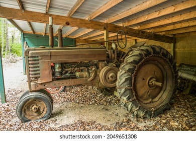 Large Rusted Vintage Farm Tractor Sitting In A Open Shed With Flat Tires No Longer In Use Discarded And Forgotten Closeup View