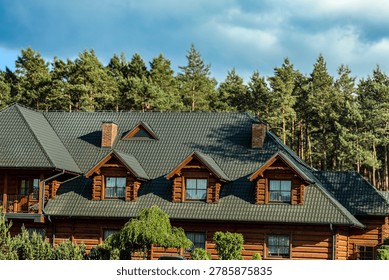A large, rustic log cabin with multiple dormer windows and brick chimneys is surrounded by a dense forest of evergreen trees
