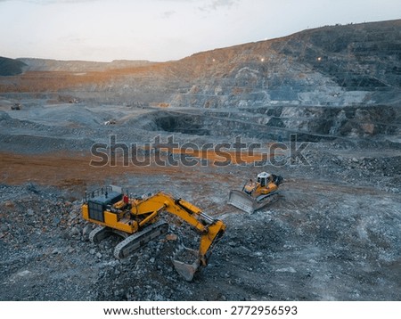Large scale open pit mining operation with excavators and bulldozers at dusk, aerial view.