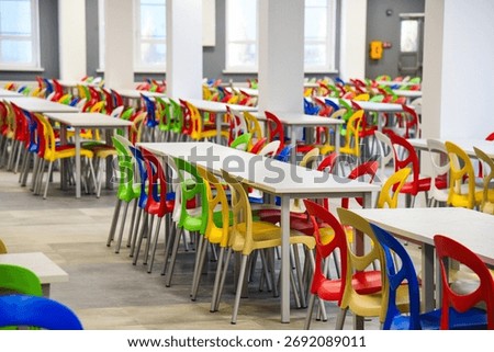 A large school cafeteria with long rows of tables and colorful chairs. The modern school canteen is ready to receive visitors