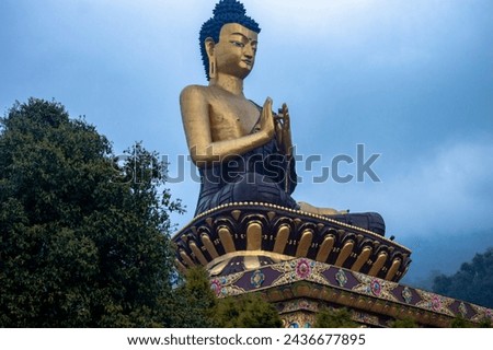 A large seated Buddha statue with an ornately decorated base and a serene facial expression. The Buddha figure is depicted in a meditating posture, with hands folded in the lap