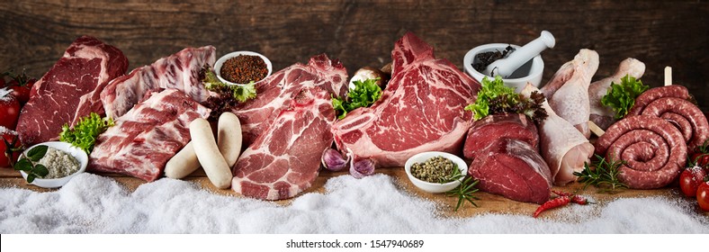 Large Selection Of Prime Raw Meat For A Winter BBQ In A Panorama With Pork, Beef, Chicken, Steak And Sausages In A Row On Snow With Fresh Herbs And Spices Suitable For Butchery Advertising