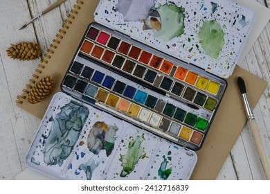 Large set of watercolor paints on a wooden table. View of the object from above. Accessories for the artist's drawing. Paints, sketchbook, brushes. - Powered by Shutterstock