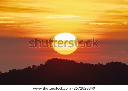 Large setting sun with visible texture behind a dark hill and a colorful sky