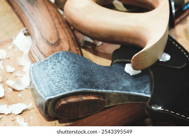 A large, sharp axe with a wooden handle in a leather sheath lies on a wooden table. handle is skillfully carved and has a natural, rustic look. The table is made of wood and has a few small scratches. - Powered by Shutterstock